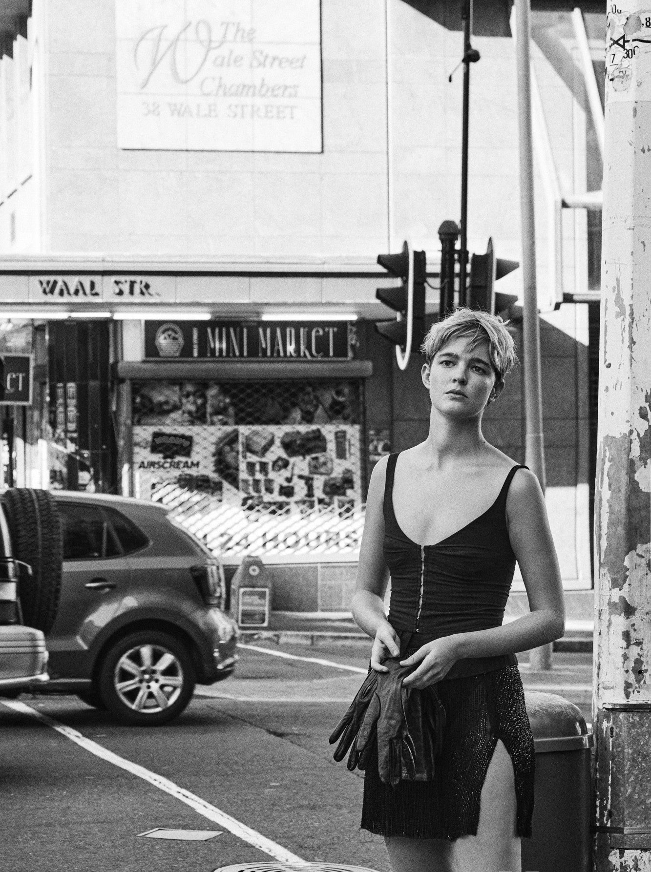 A woman in a short skirt and boots standing on a street corner, exuding confidence and style.