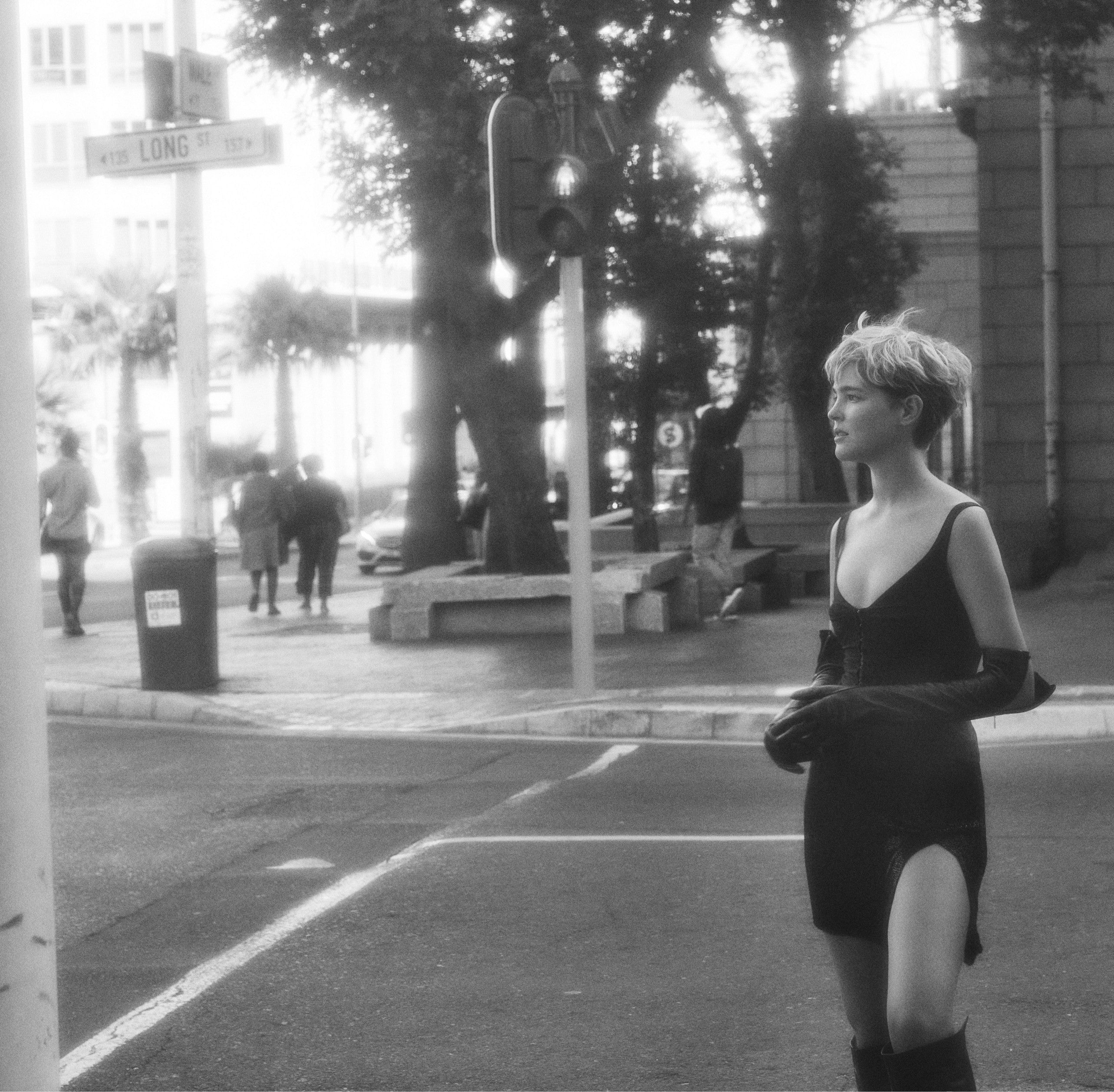 A woman in a short dress and boots standing on a street corner, exuding confidence and style.